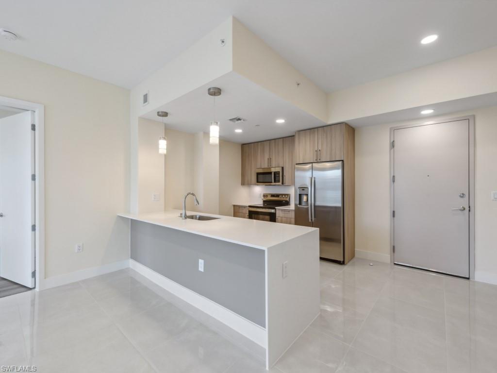 Contemporary kitchen featuring a large white quartz island with an undermount sink and three pendant lights, stainless steel appliances, wood-finish cabinetry.