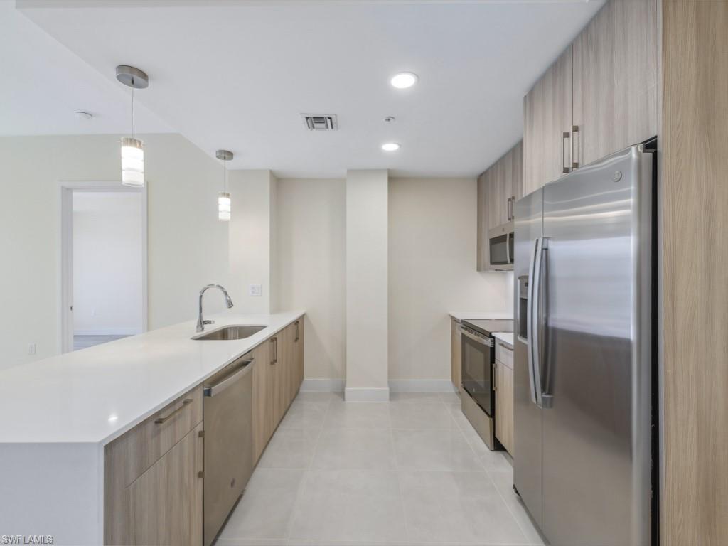 Contemporary kitchen featuring white quartz countertop island, stainless steel appliances, wood-finish cabinetry,  and pendant fixtures