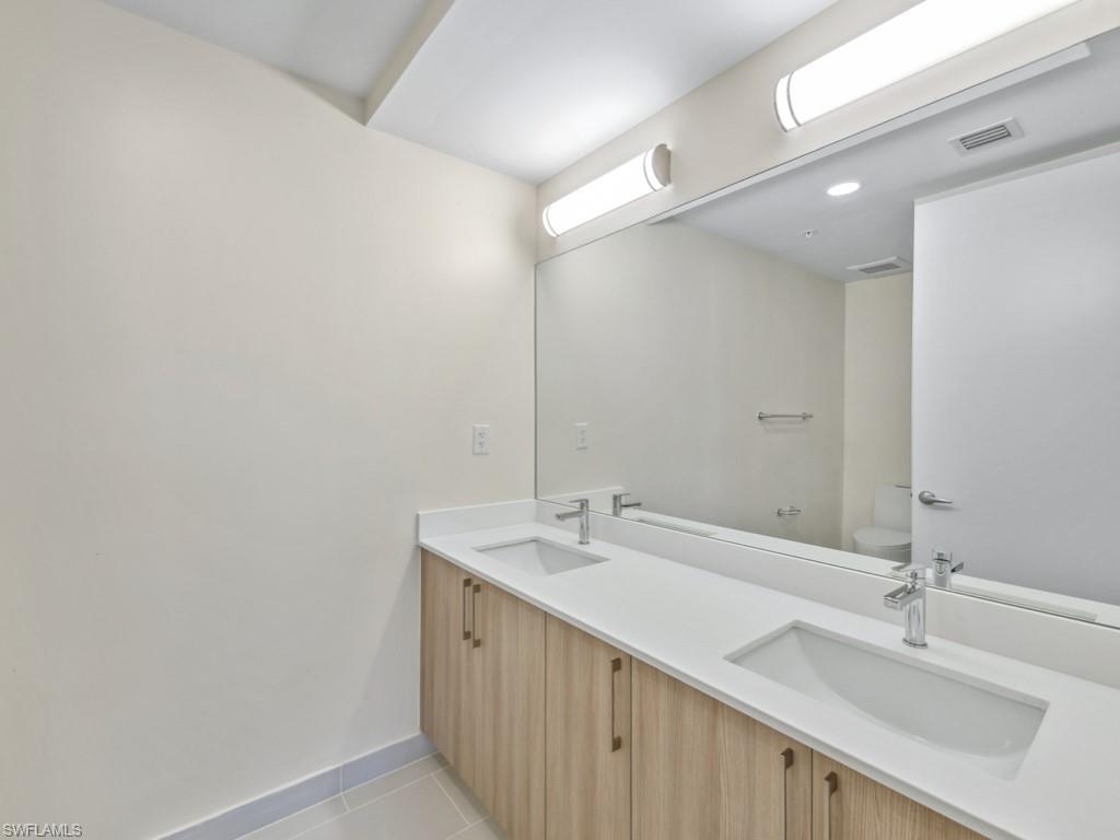 Double vanity with wood-finish cabinetry, white quartz countertops, and integrated rectangular sinks