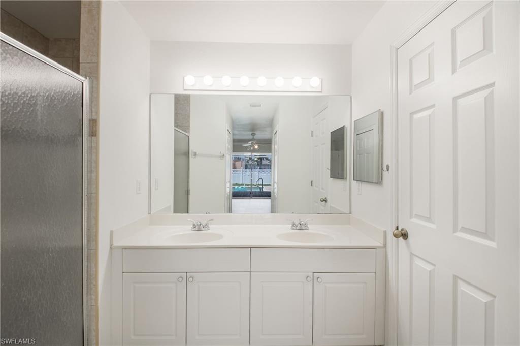 Bathroom featuring a dual vanity with white cabinetry and integrated sinks, a large wall-mounted mirror, and overhead strip lighting