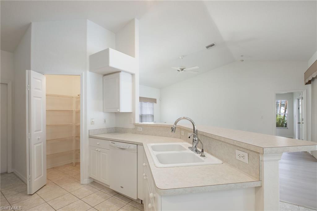 Kitchen featuring a double basin sink with gooseneck faucet, light-toned countertops, white cabinetry, integrated dishwasher, and tile flooring