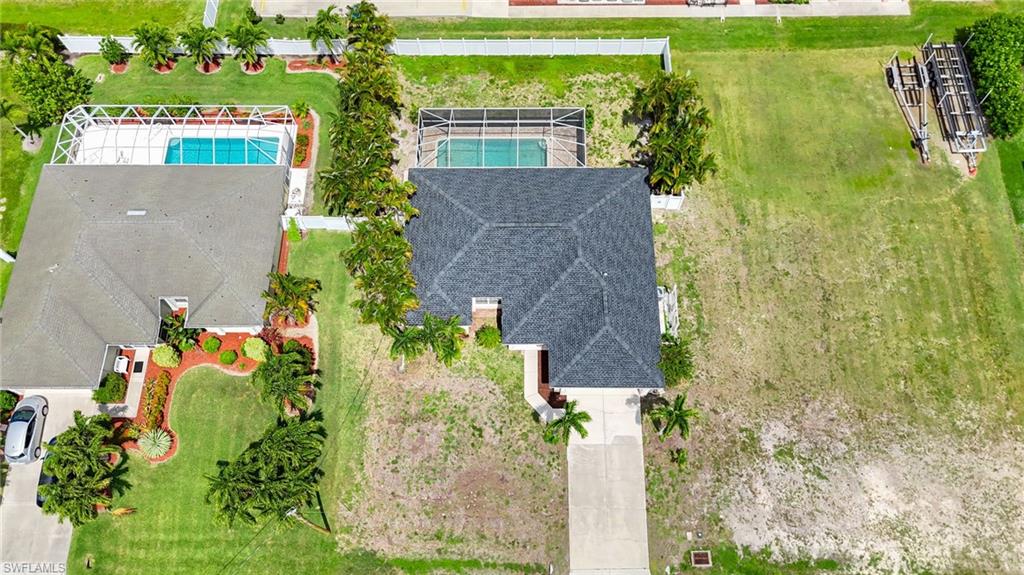 Overhead image of property featuring a dark shingle roof, attached garage, concrete driveway, pool, fence