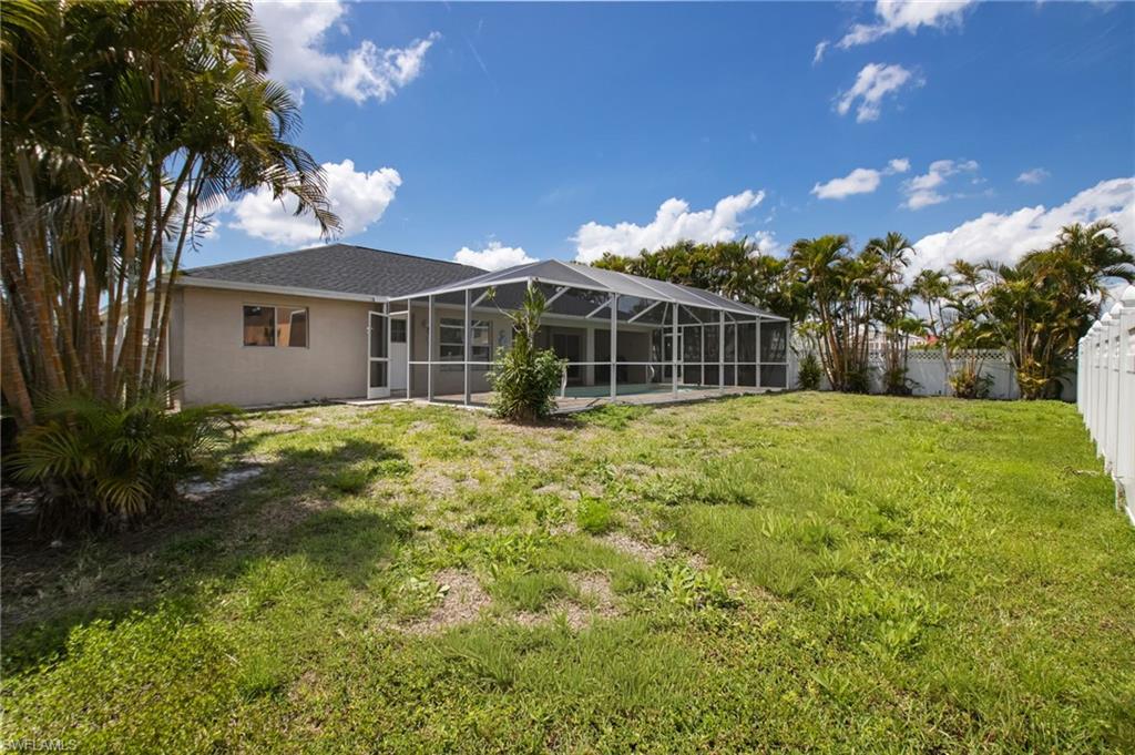Expansive backyard featuring a screened-in patio enclosure, a privacy fence, and mature palm trees