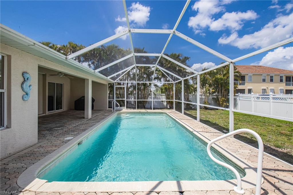 Screened outdoor pool area featuring a rectangular pool, paver deck, covered patio with sliding glass doors, and a white privacy fence