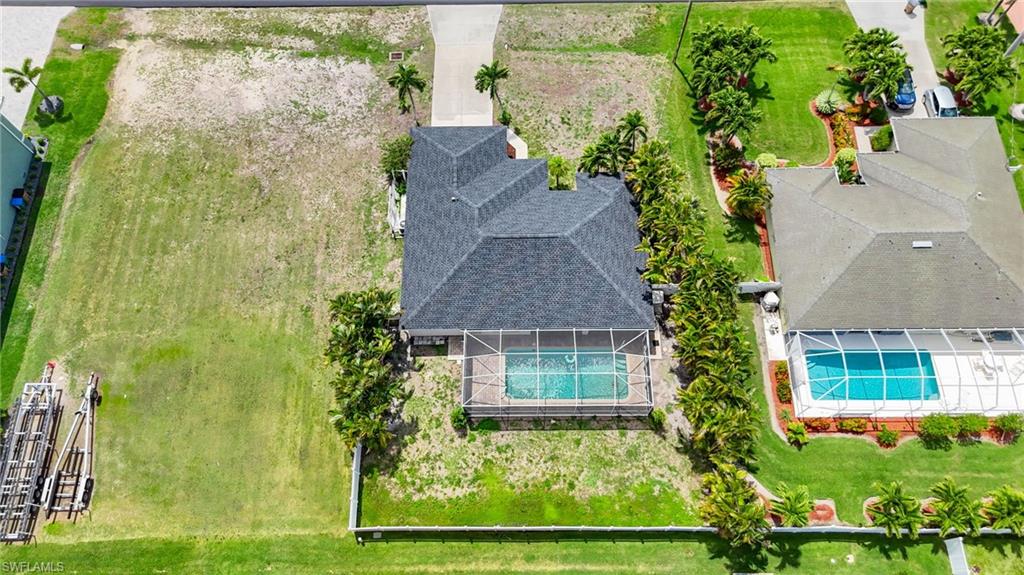 Aerial perspective showcasing a property with a screened pool enclosure and adjacent undeveloped land parcel