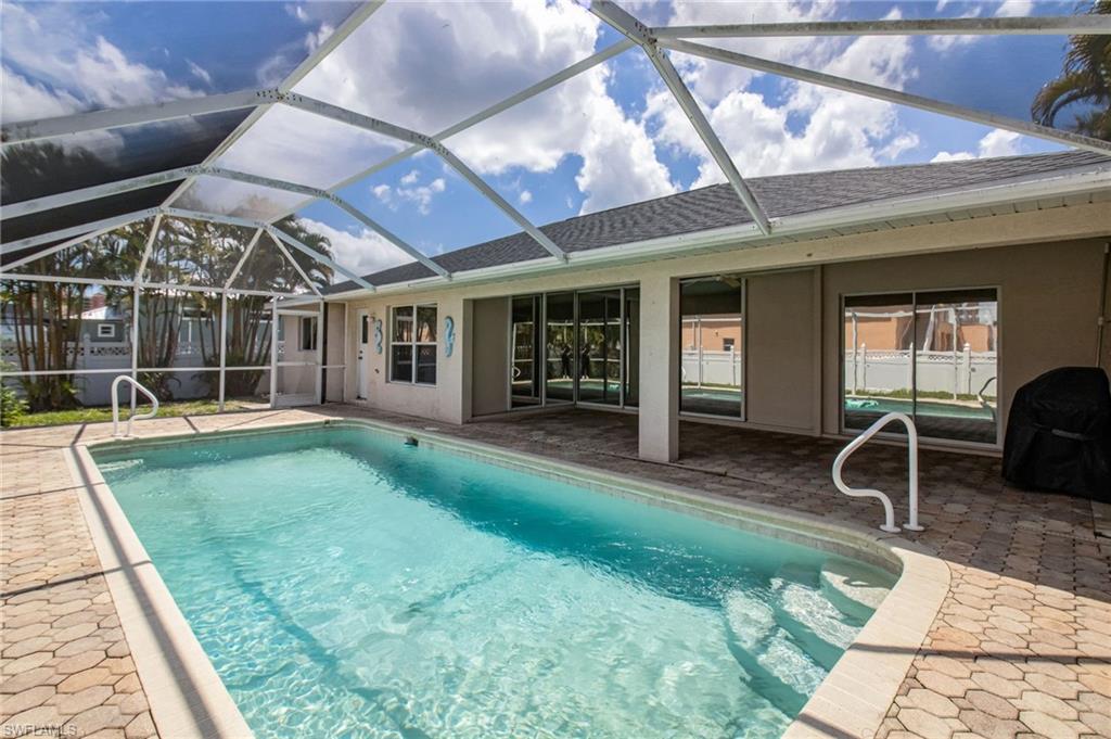 Screened pool enclosure featuring a rectangular pool with integrated steps, brick paver decking, and direct access to the interior via sliding glass doors