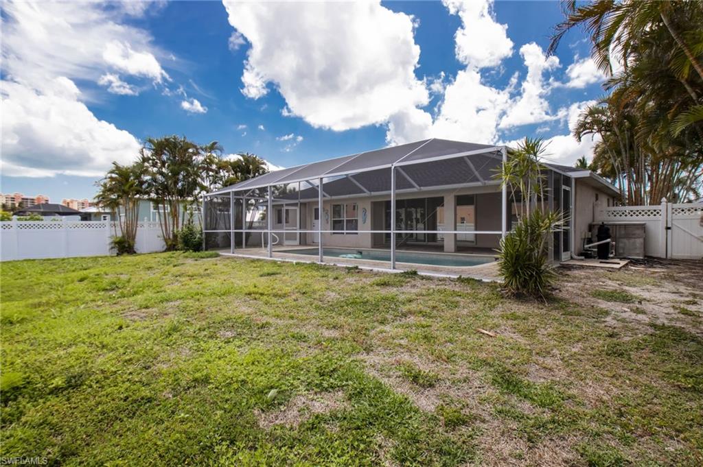 Expansive backyard with a screened pool enclosure, concrete patio, and a white privacy fence