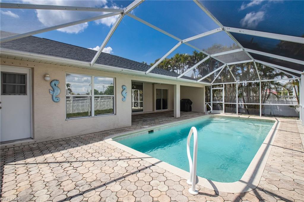 Screened-in pool area featuring a rectangular swimming pool with a white handrail, surrounded by a paver patio