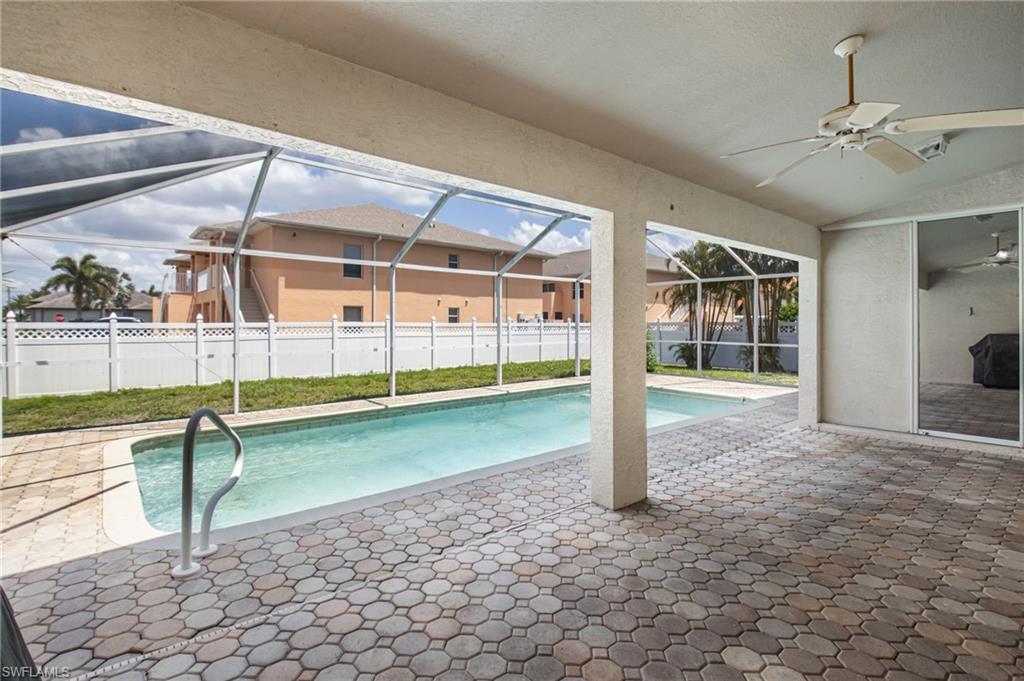 Screened-in patio area featuring a rectangular swimming pool with a handrail, paver decking, and a ceiling fan