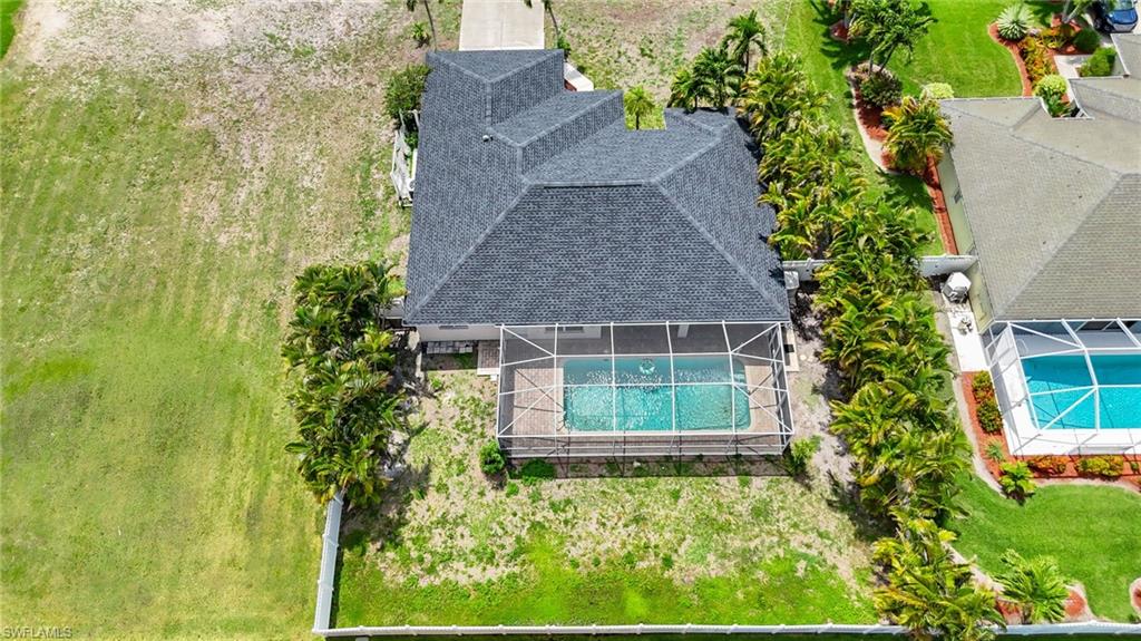 Aerial view of a residential property featuring a screened-in swimming pool and a dark shingle roof