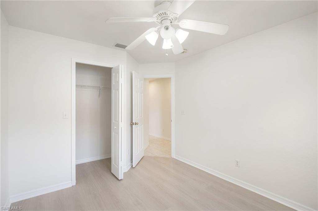 Bright room featuring a ceiling fan with integrated lighting, clean white walls, and light wood-finish flooring