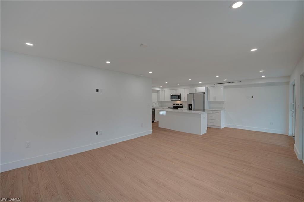 Open-concept living area with wood-finish flooring, recessed lighting, and white baseboards