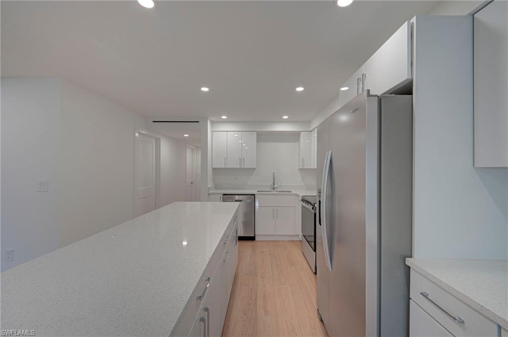 Modern kitchen featuring an extended island with a light-toned countertop, stainless steel appliances, and wood-finish flooring