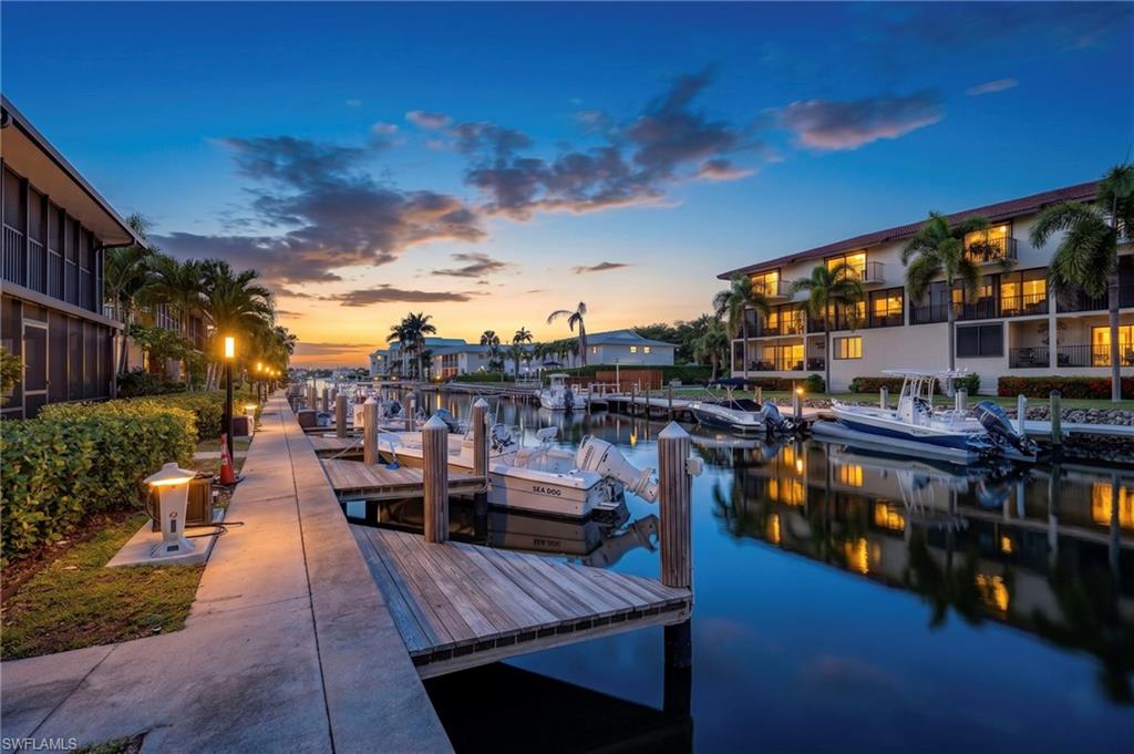 Waterfront property featuring multiple boat slips, a concrete walkway, established landscaping, and palm trees