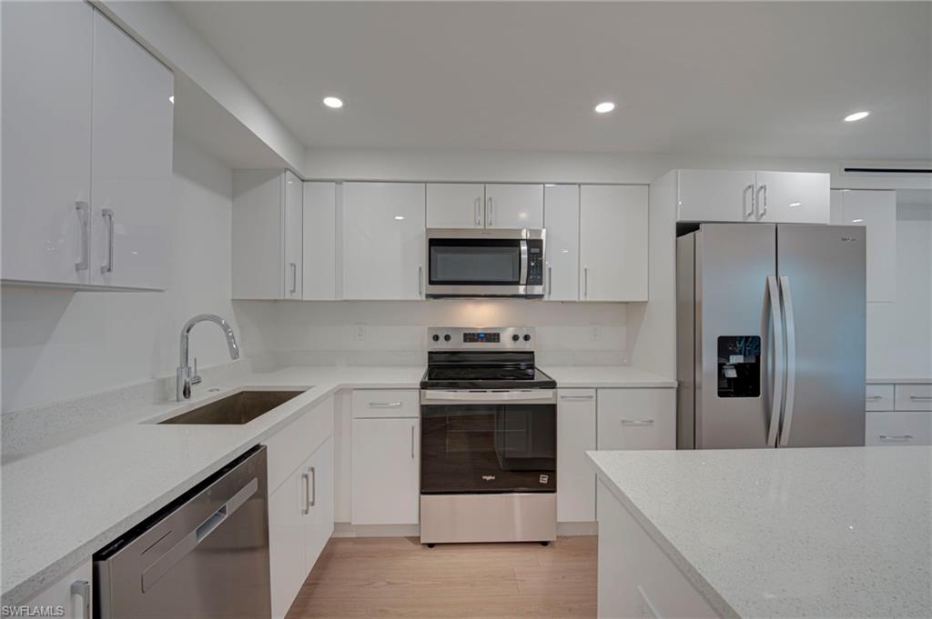 Modern kitchen featuring white glossy cabinetry, light-toned countertops, and stainless steel appliances including a refrigerator, range, microwave, and dishwasher