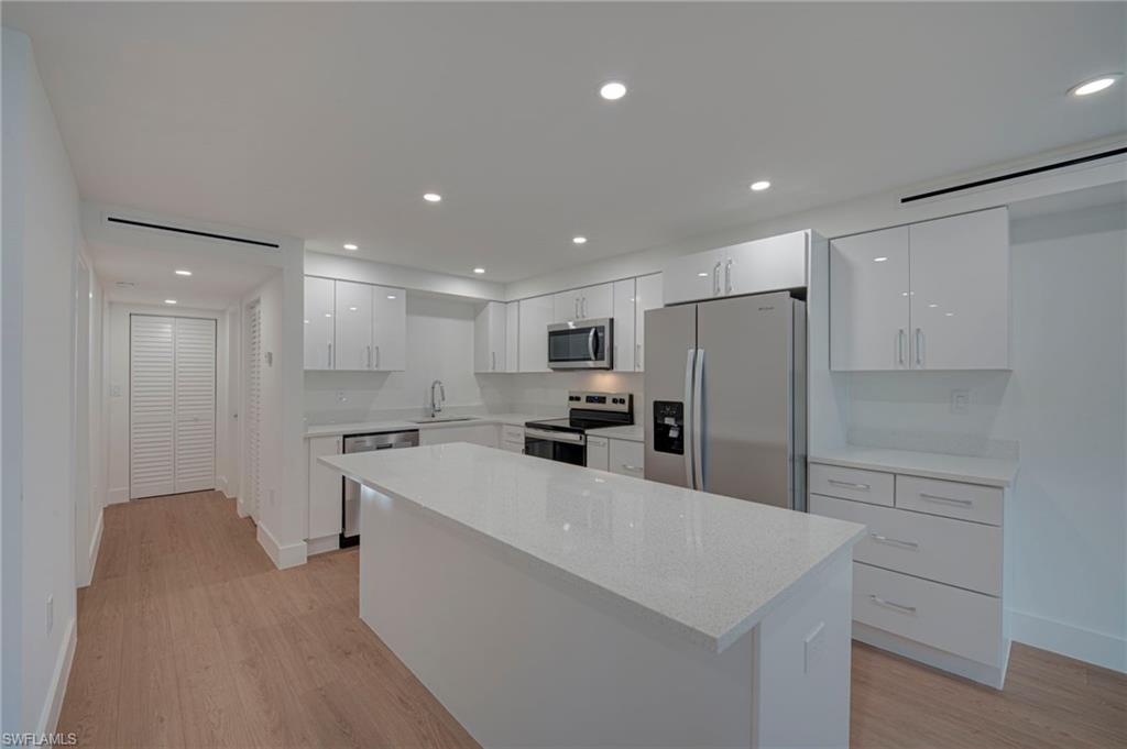 Contemporary kitchen featuring a large center island with a light-toned countertop, white high-gloss cabinetry, stainless steel appliances, and wood-finish flooring
