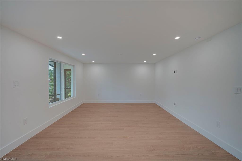 Spacious room featuring wood-finish flooring, recessed lighting, and white baseboards