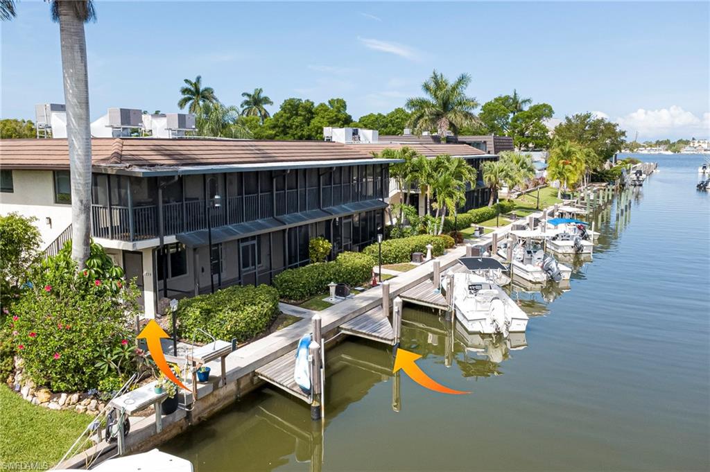 Waterfront property featuring multiple boat slips, a long private dock, screened-in balconies, tropical landscaping, and tile roofing