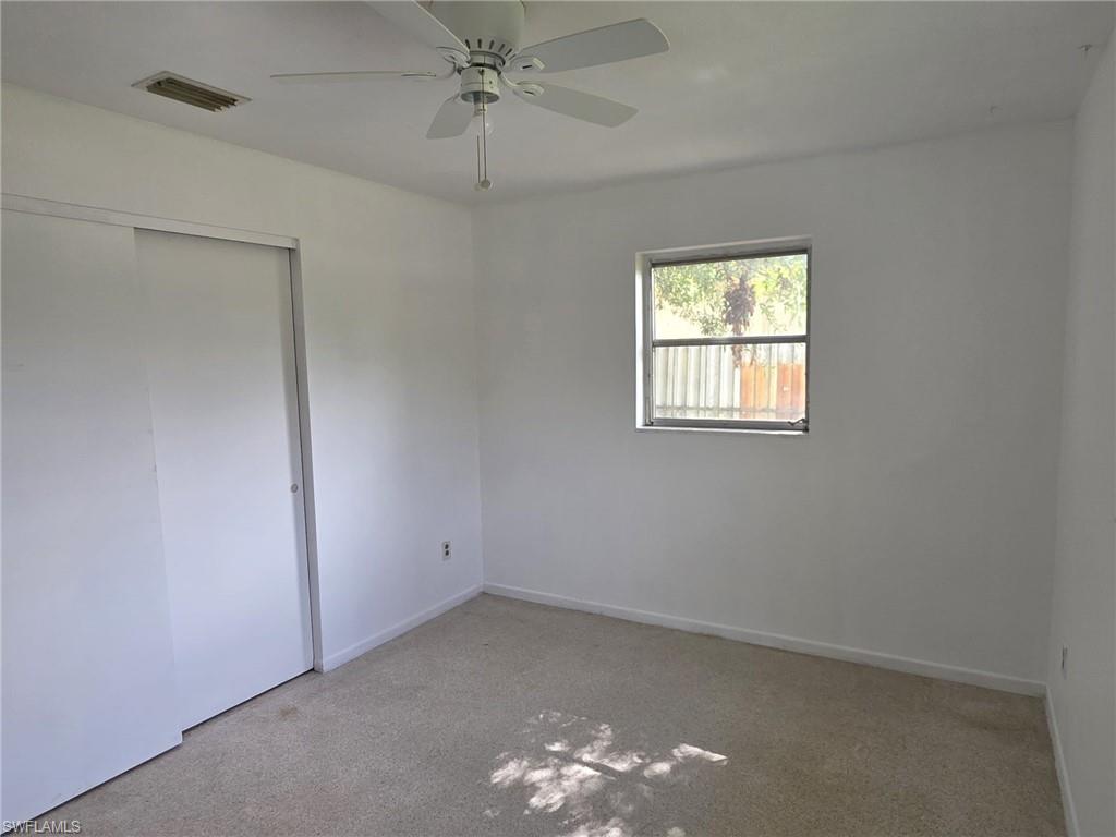 Neutral-toned carpeting paired with white walls, featuring a ceiling fan and a window