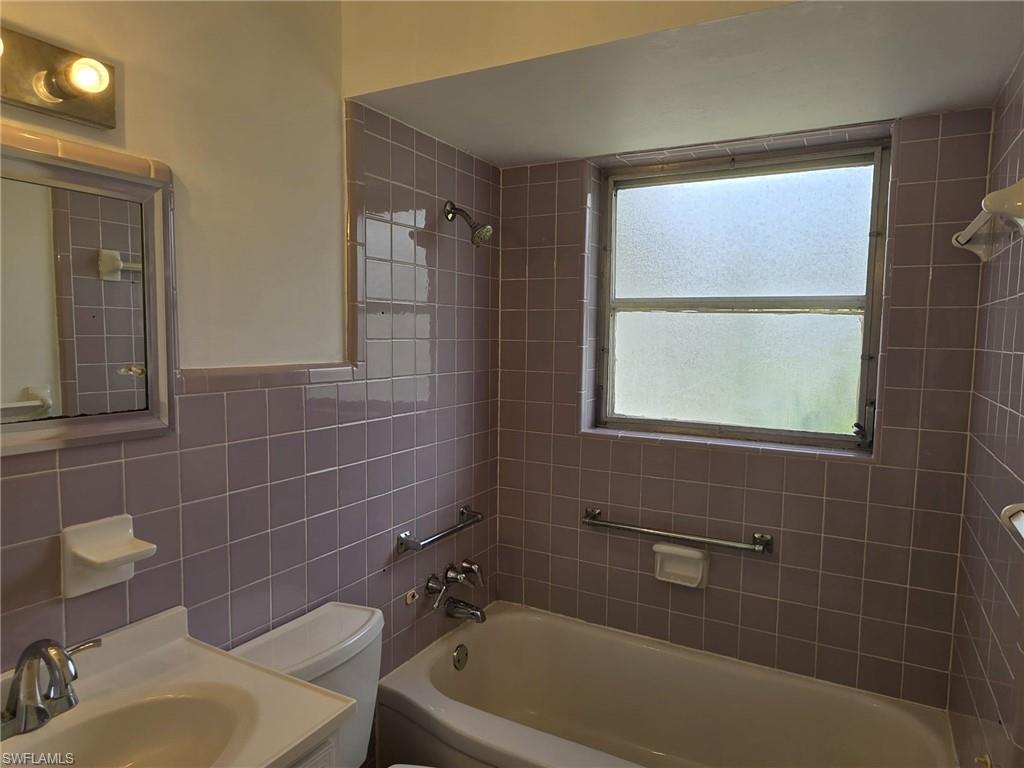 Bathroom featuring lavender ceramic tile walls and a built-in bathtub with shower fixture