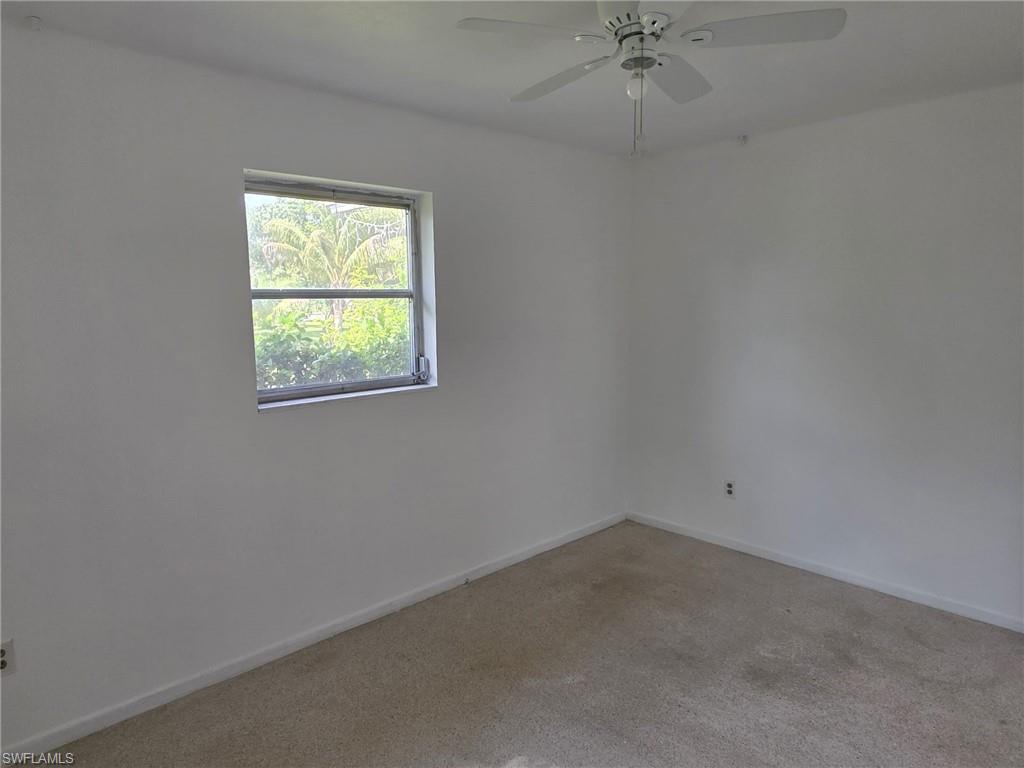 White interior walls with a single window, a ceiling fan with integrated lighting, and carpeted flooring