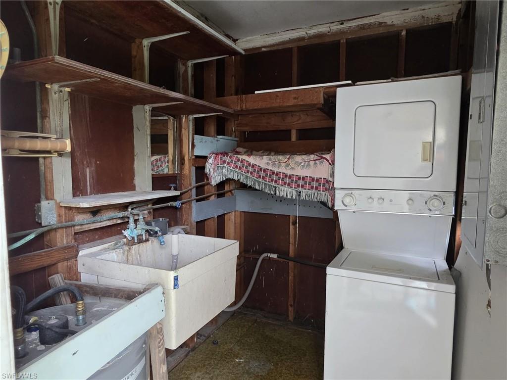Utility area featuring a stackable washer and dryer, a wall-mounted utility sink with exposed plumbing, and multiple built-in wood shelves