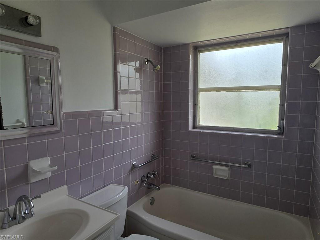 Bathroom featuring lavender wall tile, a bathtub, and a vanity with an integrated sink