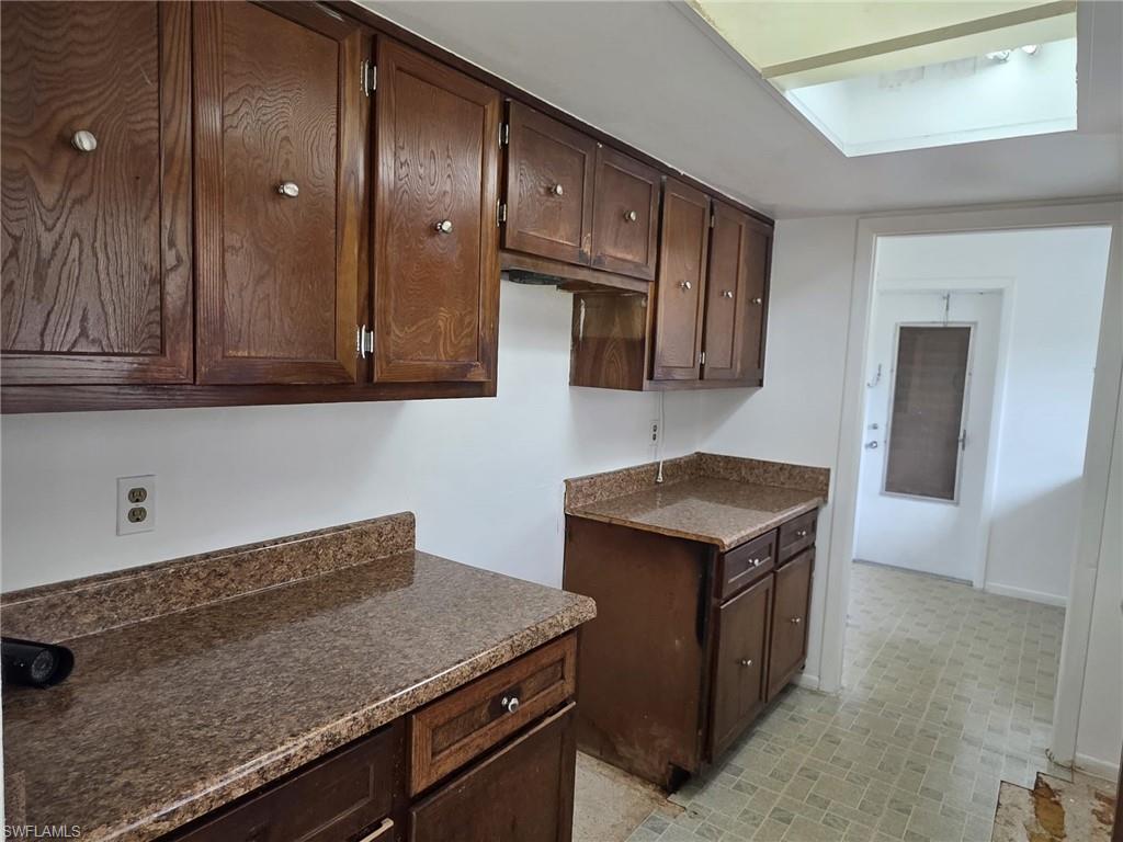 Kitchen featuring wood-finish cabinetry with silver-tone hardware, speckled countertops with a matching backsplash, and a ceiling-mounted skylight