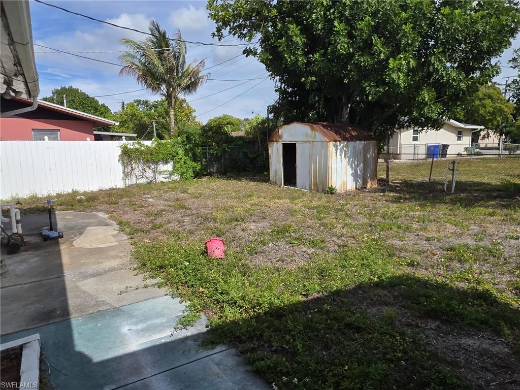Expansive backyard featuring a concrete patio, white privacy fence, mature trees, and a utility shed