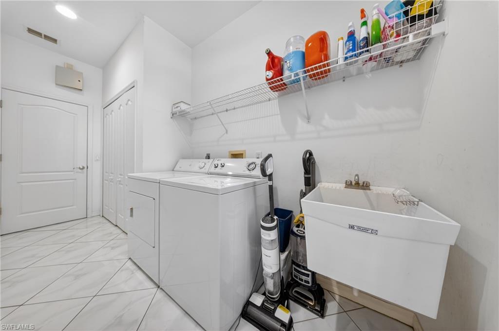 Laundry area featuring white tile flooring, a wall-mounted utility sink, and overhead wire shelving