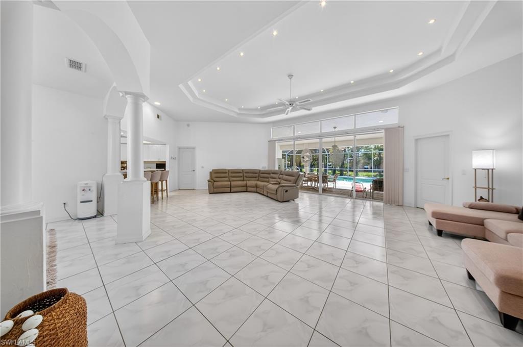 Spacious living area featuring large format tile flooring, a tray ceiling with recessed lighting, and expansive sliding glass doors