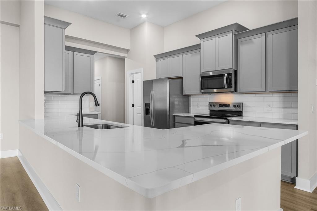 Kitchen featuring gray cabinetry, light wood finished floors, a peninsula, and decorative backsplash