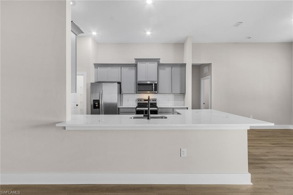 Kitchen featuring gray cabinets, stainless steel appliances, decorative backsplash, light stone counters, and light wood-type flooring