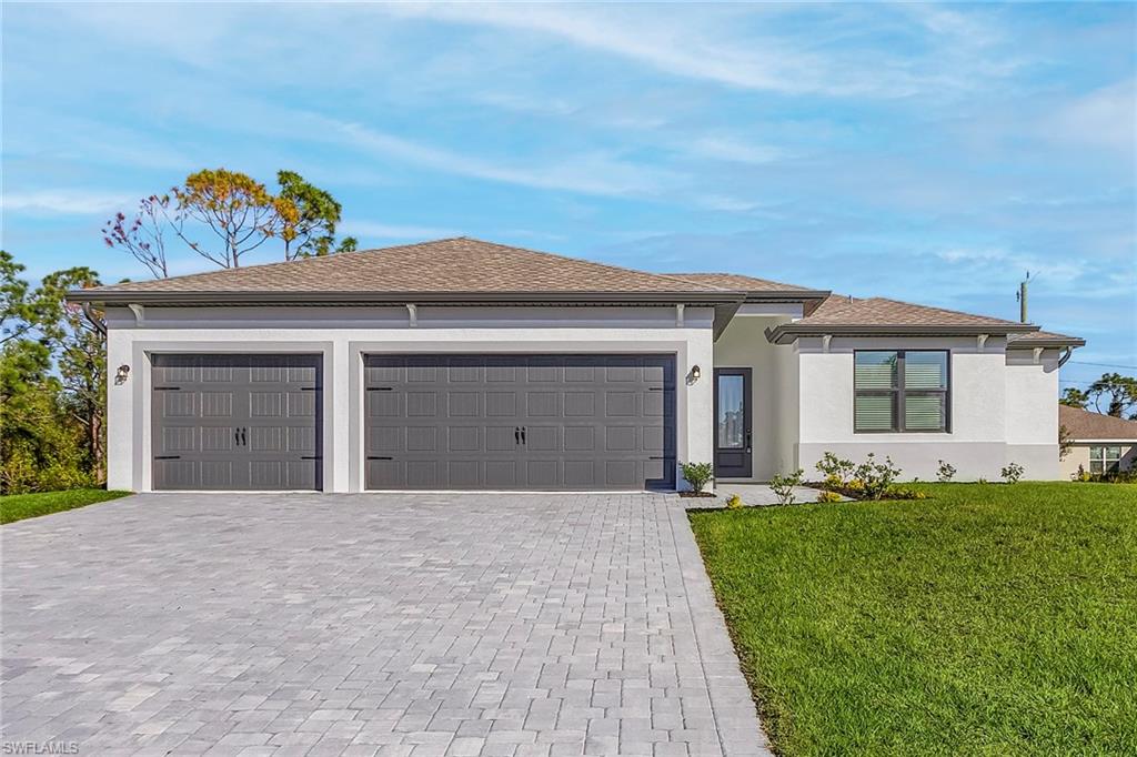Prairie-style home featuring a front yard, decorative driveway, stucco siding, an attached garage, and roof with shingles