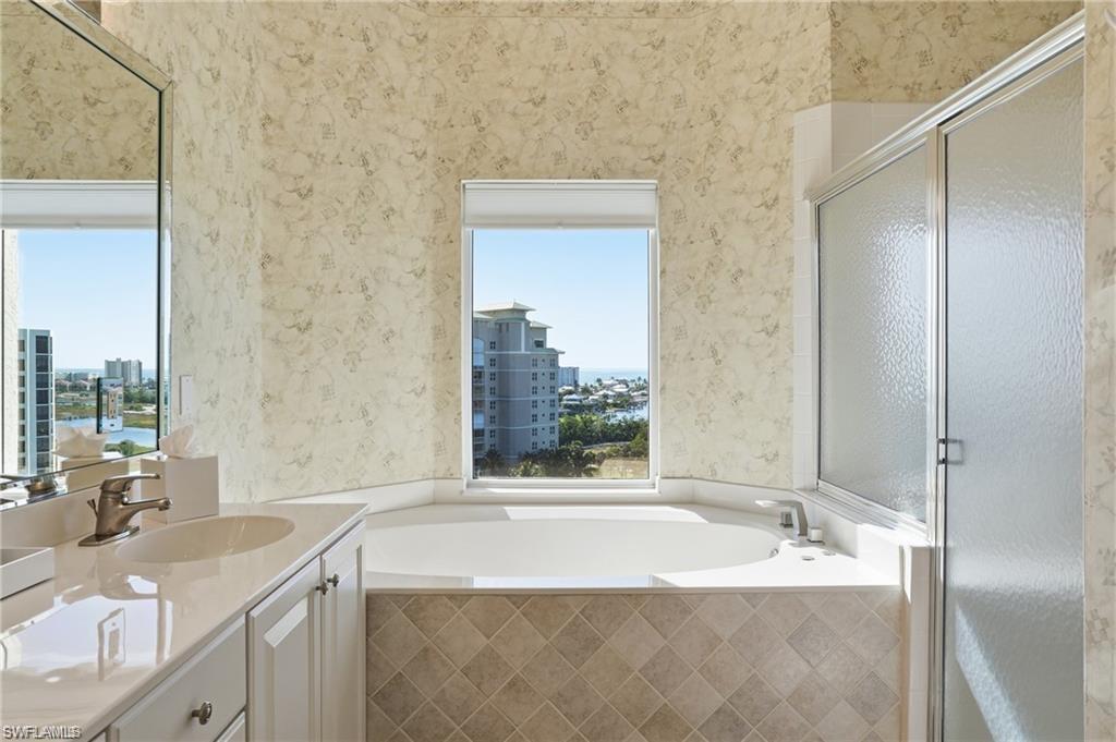 Bathroom featuring a built-in soaking tub, separate shower enclosure with frosted glass, and a vanity with an integrated sink and light-colored countertop