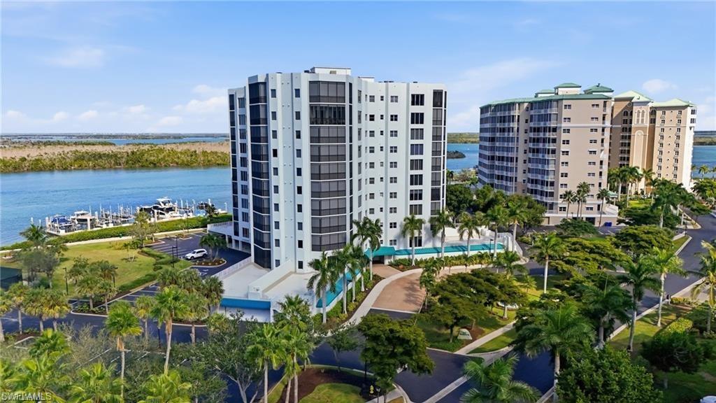 Waterfront high-rise building featuring multiple balconies, a circular drive, and lush tropical landscaping