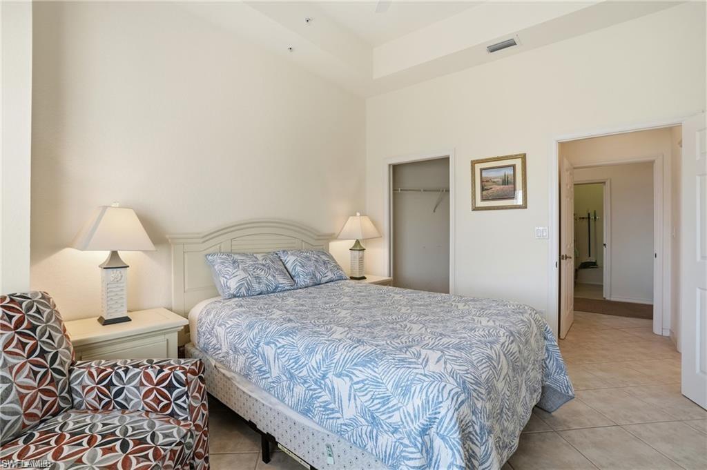 Tray ceiling bedroom featuring tile flooring, a built-in closet, and an entry to a separate room with tile flooring