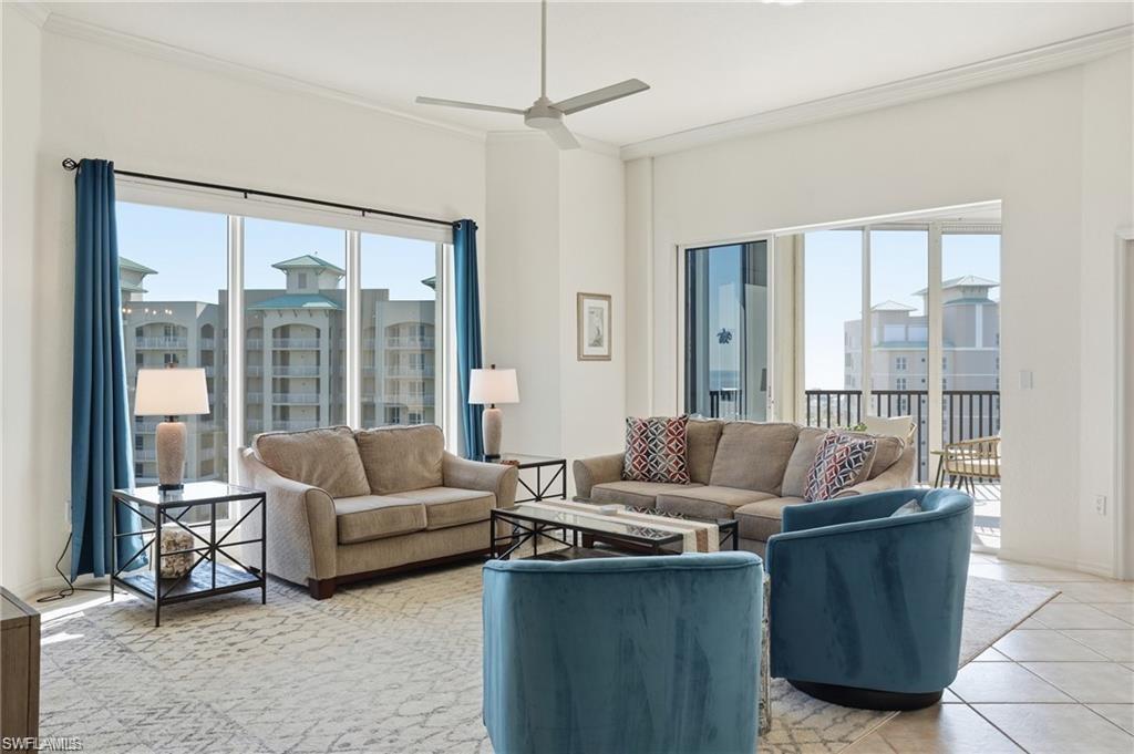 Spacious living area featuring large windows, a sliding glass door leading to a balcony, high ceilings with crown molding, and a ceiling fan