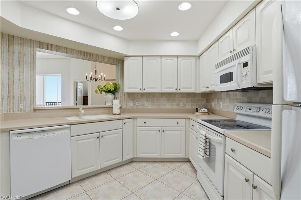 White kitchen featuring extensive cabinetry, integrated appliances, recessed lighting, and a pass-through window