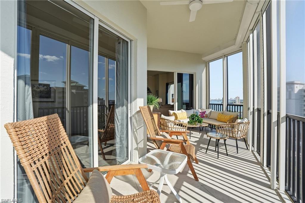 Expansive covered balcony featuring a ceiling fan, sliding glass doors, vertical privacy screens, and metal railings