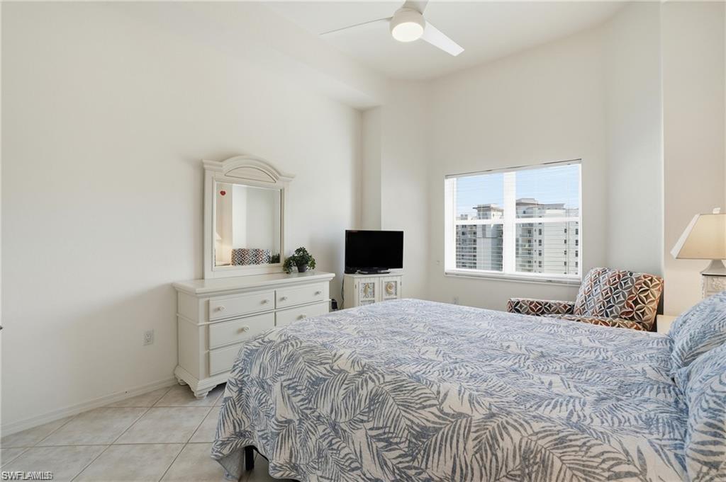 Bright bedroom with large window, tile flooring, high ceilings, and a ceiling fan