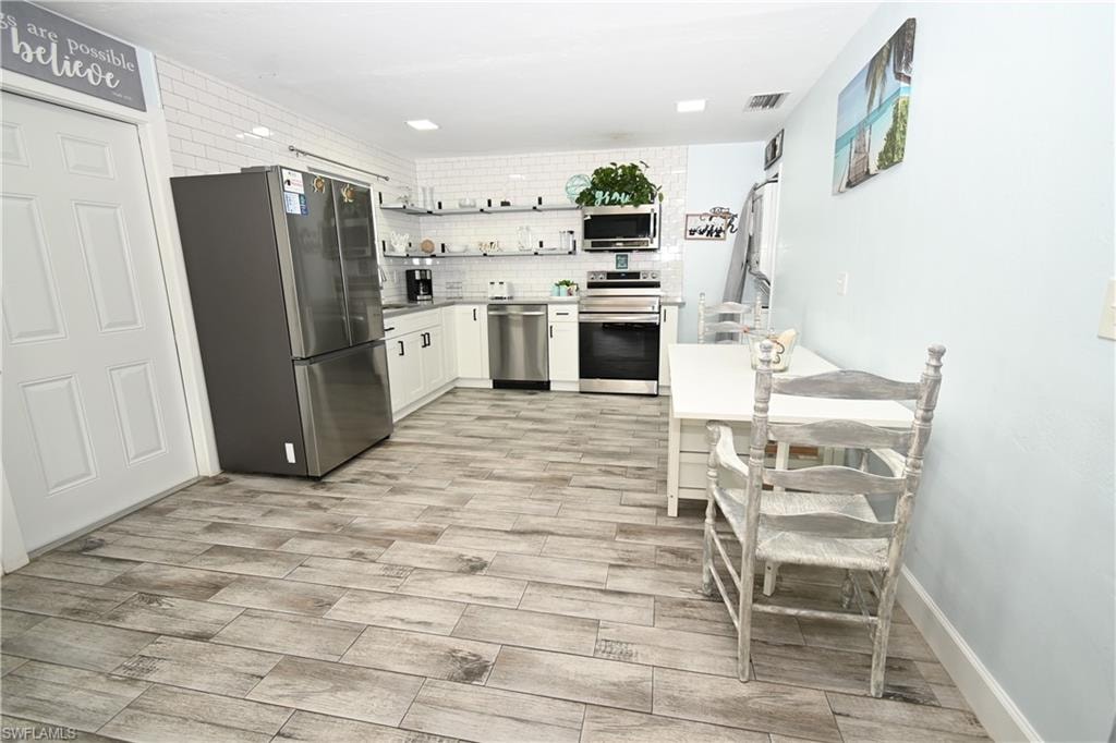 Kitchen featuring wood-finish tile flooring, white shaker cabinetry, stainless steel appliances, and a subway tile backsplash