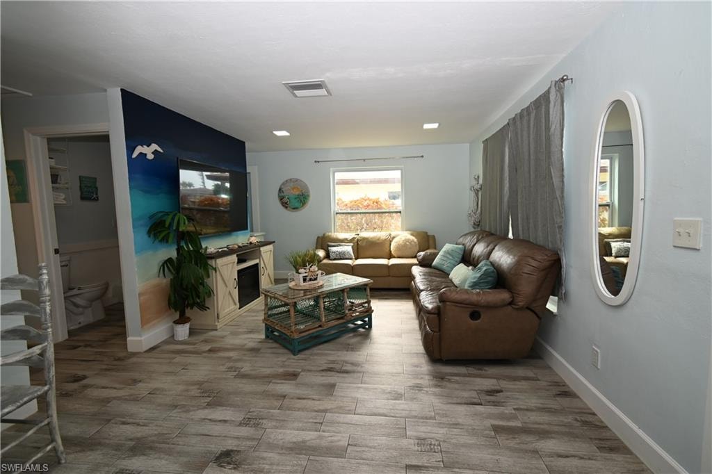 Spacious living area featuring wood-finish tile flooring, recessed ceiling lighting, and a console with an integrated electric fireplace