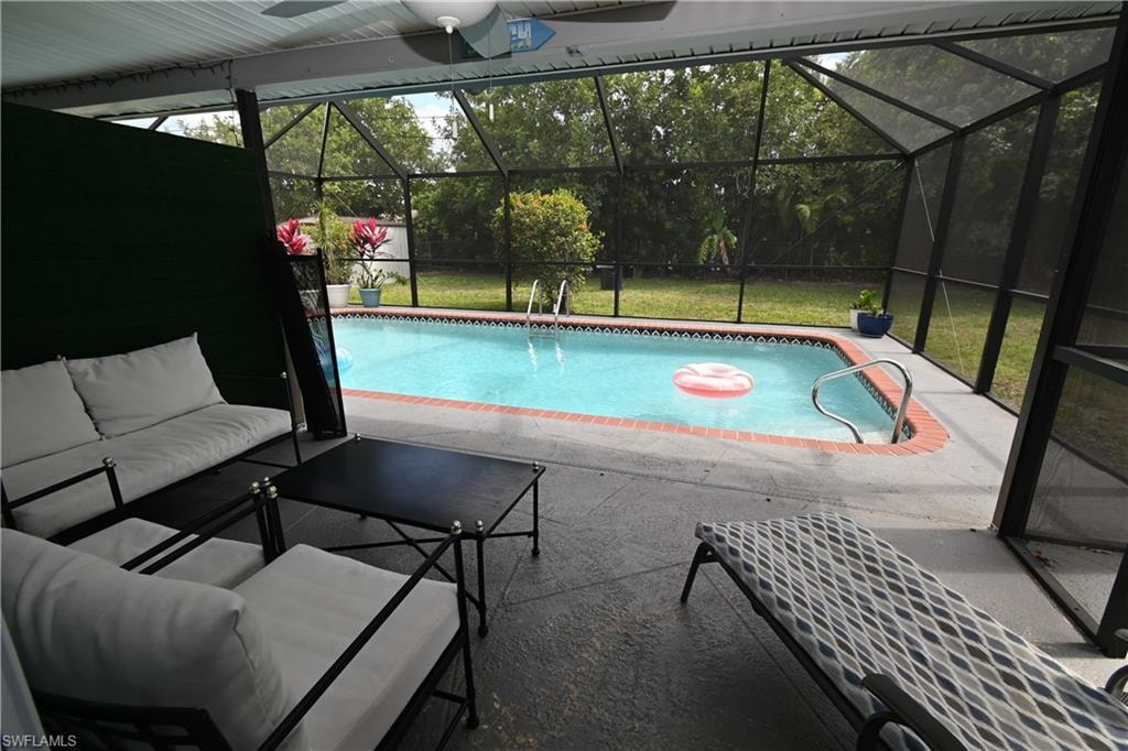 Screened outdoor living area featuring a pool with concrete decking, brick coping, and stainless steel handrails