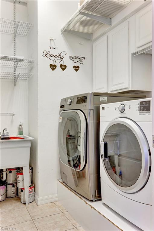 Dedicated laundry area featuring a utility sink, white upper cabinetry, and tile flooring
