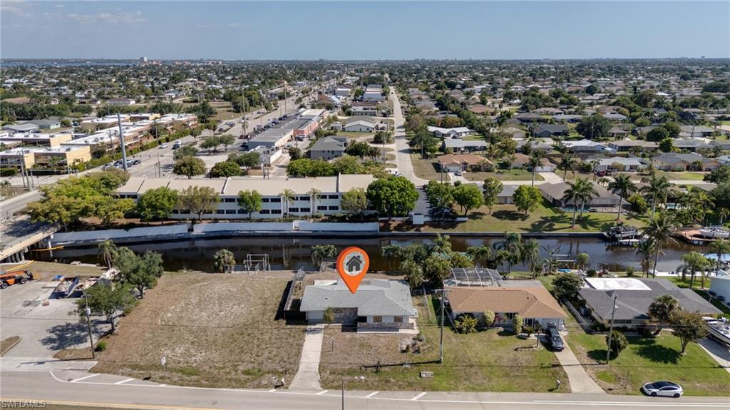 Aerial view of a residential property featuring a single-story structure with a gray roof and concrete driveways, situated on a lot with undeveloped green space