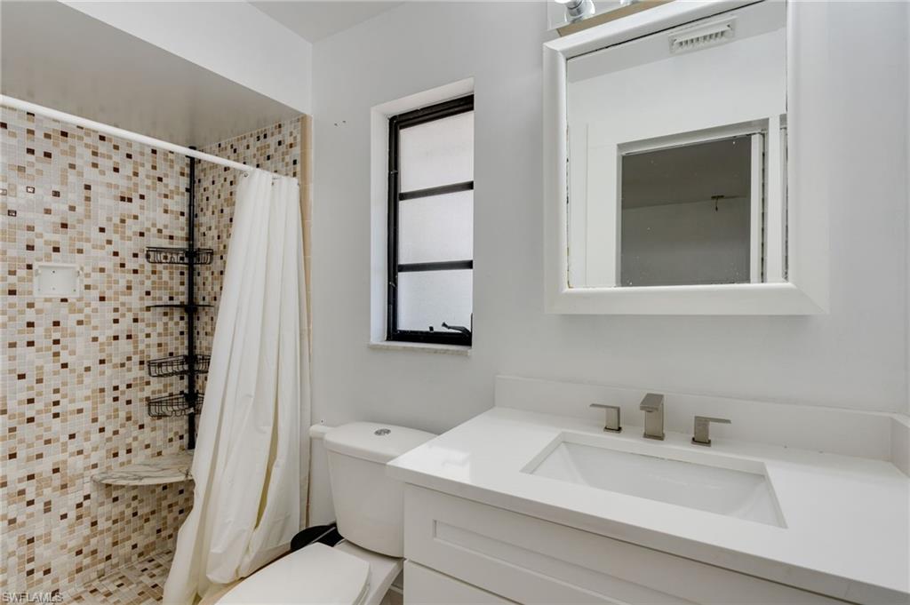 Bathroom featuring a tiled shower with a built-in seat, a white vanity with an integrated sink, a rectangular framed mirror, and a fixed window