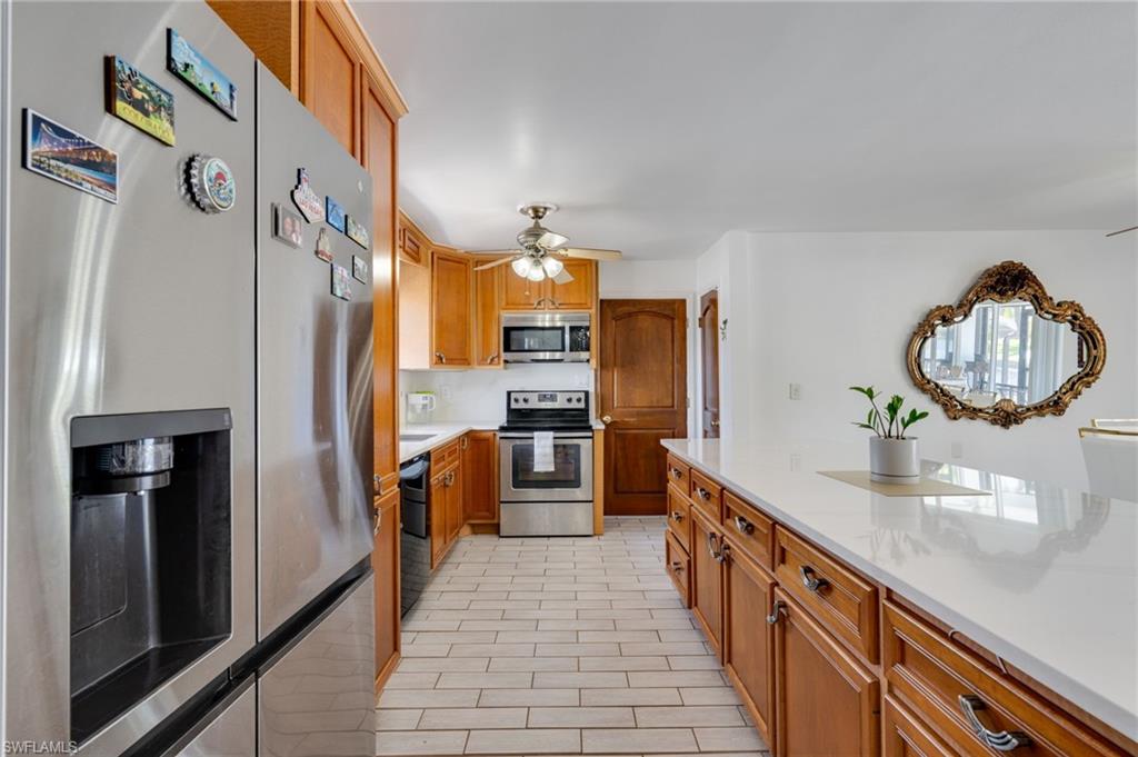 Kitchen featuring a central island with a white countertop and wood-finish cabinetry, stainless steel appliances including a refrigerator and range with microwave, light-colored tile flooring, and a detailed mirror accent