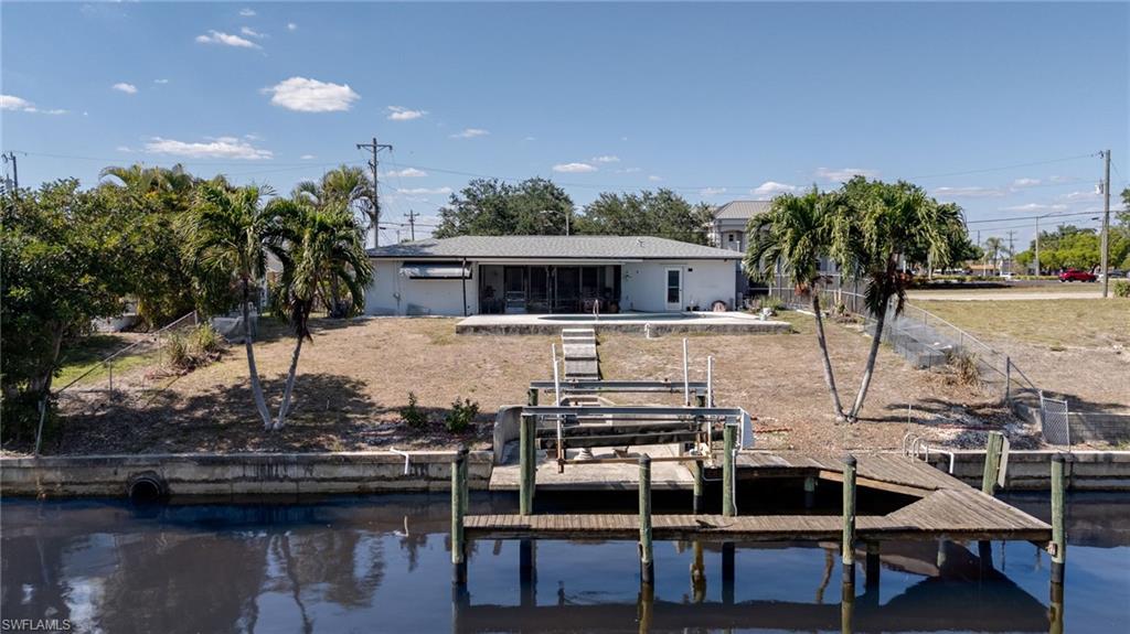 Waterfront property featuring a private dock with a boat lift, concrete seawall, and mature palm trees
