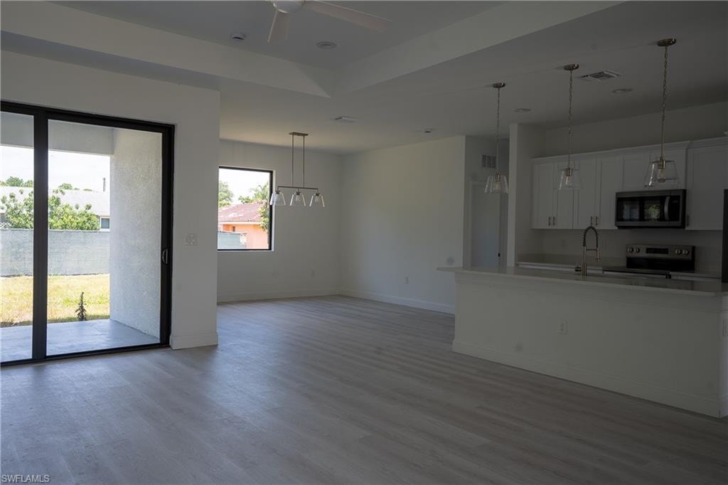 Open-concept living area featuring light wood-finish flooring, a kitchen island with pendant lighting, white cabinetry, and stainless steel appliances